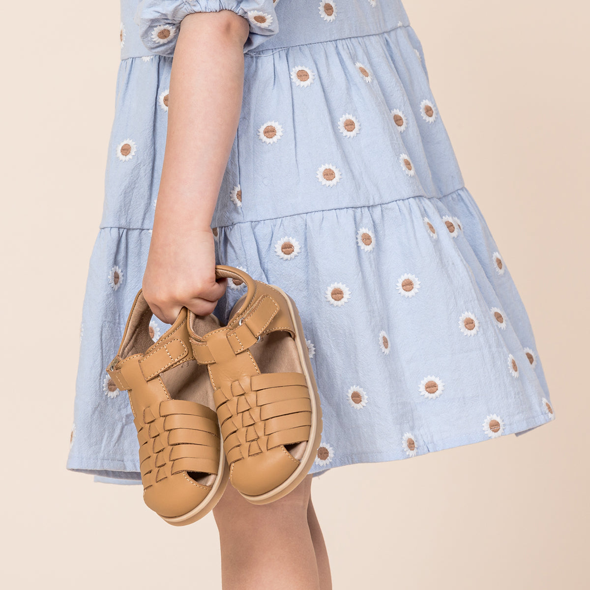 Toddler girl holding pretty brave tan sandals